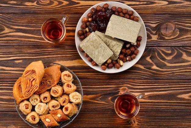 Premium Photo Assorted Traditional Eastern Desserts With Tea On Wooden Background Arabian Sweets On Wooden Table Baklava Halva Rahat Lokum Sherbet Nuts Dates Kadayif On Plates Space For Text