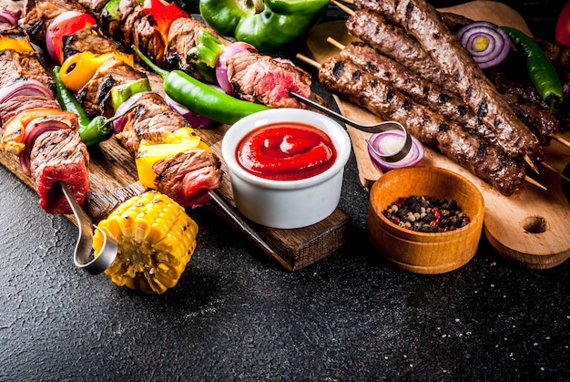 Assortment various barbecue food grill meat, bbq party fest - shish kebab, sausages, grilled meat fillet, fresh vegetables, sauces, spices, dark rusty concrete table, above copy space Premium Photo