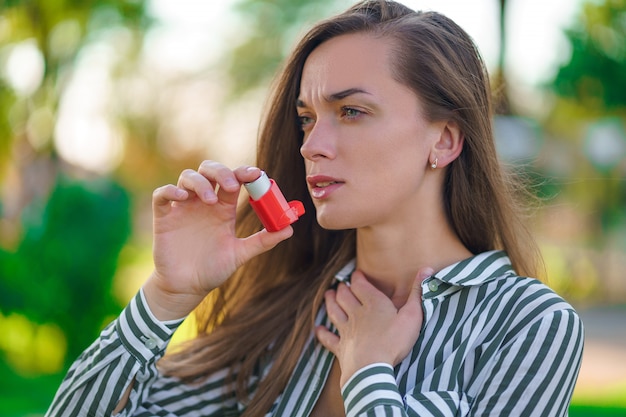 Asthmatic woman using inhaler from an asthma attack in park Premium Photo