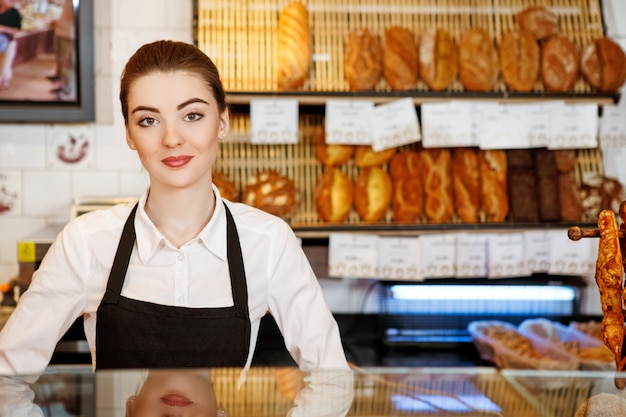 どうぞ何なりとお申し付けください 笑顔のパン屋で働く魅力的な若い女性 プレミアム写真