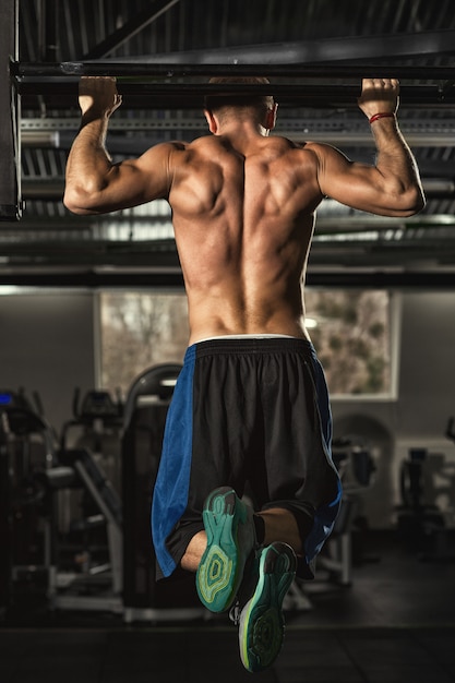 ジムで運動プルアップを行う強い引き締まった体と運動の上半身裸の男 プレミアム写真