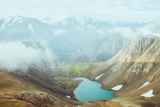 Premium Photo Atmospheric Alpine Landscape To Beautiful Glacial Lake In Highland Valley Big Snowy Mountains With Glacier Above Mountain Lake Thick Low Clouds Among Rocks Wonderful Scenery Flying Over Mountains