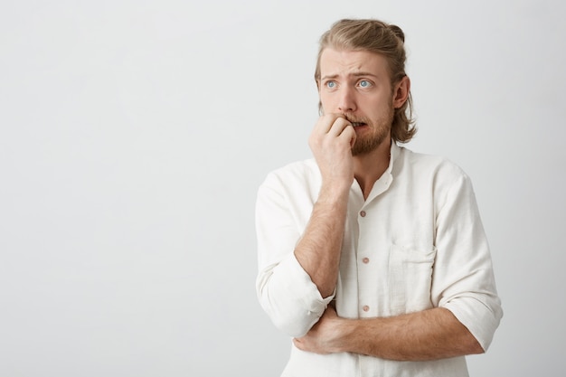 青い目と爪を噛むひげを持つ魅力的な金髪の男 無料の写真