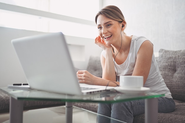 Attractive happy young student studying online at home, using laptop computer, headphones, having video chat, waving. remote work, distance education. video conference or virtual event on quarantine Premium Photo