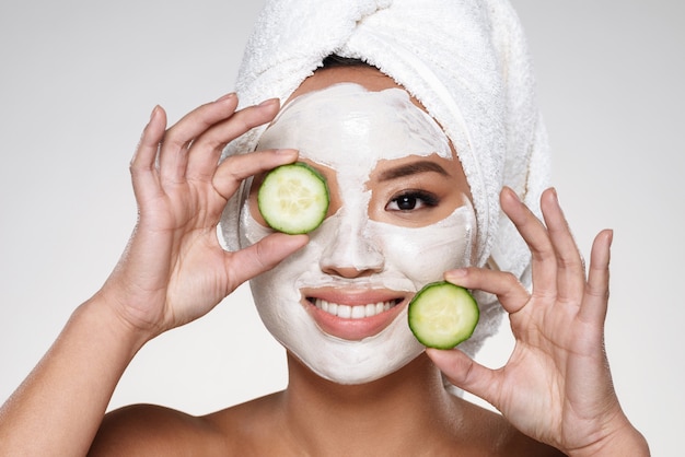 Attractive smiling lady with scrab on face holding cucumber slices Free Photo