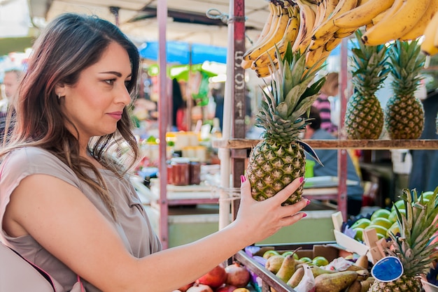 Attractive woman shopping in green market. closeup portrait beautiful young woman picking up, choosing fruits, pineapples. positive face expression emotion feeling healthy life style Free Photo