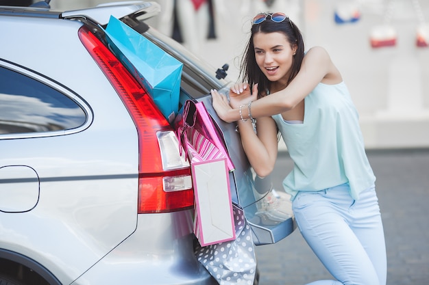 多くの小売店を車に入れようとしている魅力的な若い女の子 買い物袋を荷物に入れている女性 買い物袋をトランクに押し込む若い女性 プレミアム写真