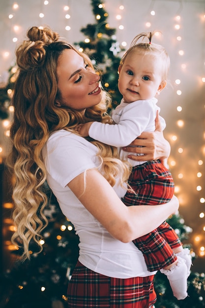 魅力的な若いお母さんは クリスマスの雰囲気の中で赤ちゃんを膝に抱きます 無料の写真