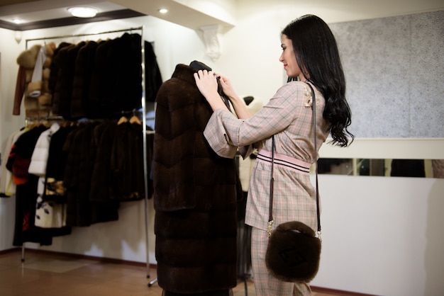 Premium Photo | Attractive young woman choosing a fur coat from the ...