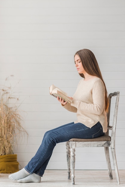 An Attractive Young Woman Sitting On Wooden Chair Reading Book