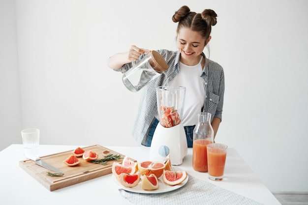 グレープフルーツとローズマリーのブレンダーで水を追加する笑顔の魅力的な若い女性 健康的なダイエット食品栄養 無料の写真