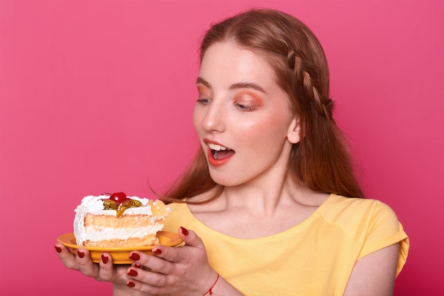 開いた口を持つ魅力的な若い女性は 手でおいしいケーキのプレートを保持しています 赤いマニキュアで茶色の髪の女性 無料の写真