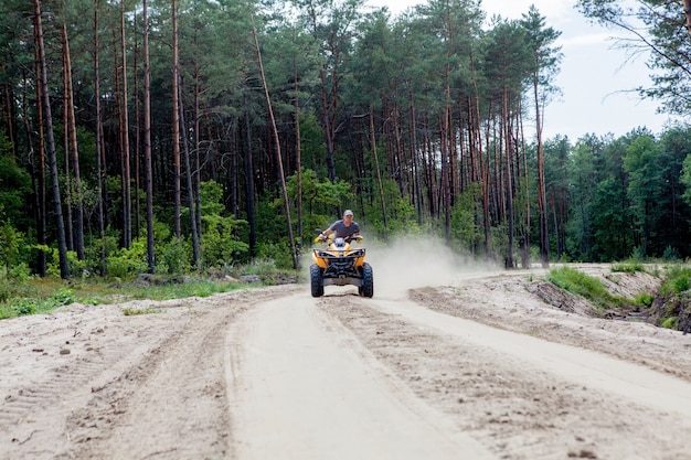 砂浜の森で黄色の四輪バギーatv全地形車両に乗る男 エクストリームスポーツモーション アドベンチャー 観光名所 プレミアム写真