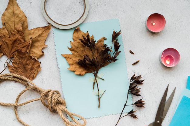 Autumn dry leaves on blue paper with string and lighted candles over the white backdrop Free Photo