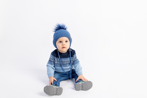暖かい冬の服と帽子 子供服 子供服の広告で白い孤立した壁に座っている赤ちゃん8ヶ月の男の子 プレミアム写真
