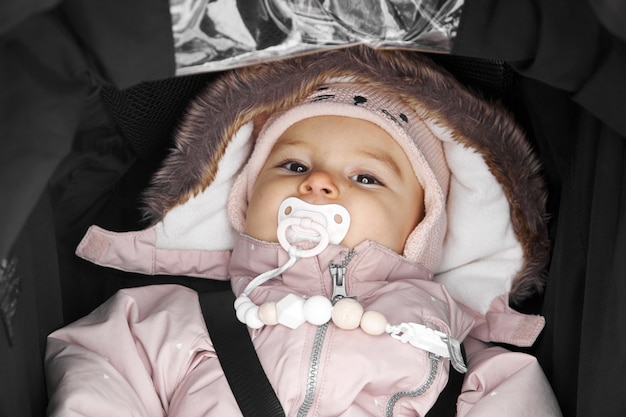Baby toddler in balck stroller outdoors on a snowy winter dayin sonwsuit Premium Photo