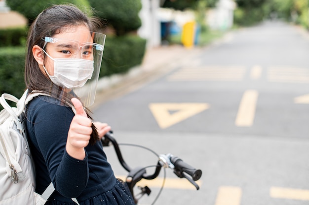 学校に戻る。フェイスマスクを着用し、自転車に乗って学校に行く親指 