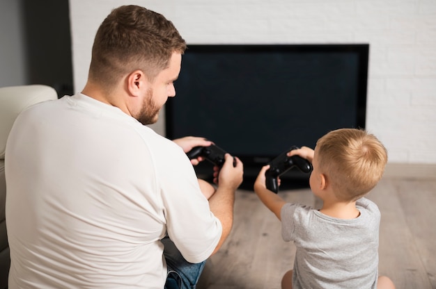 Back view father and son playing with controllers close-up Free Photo
