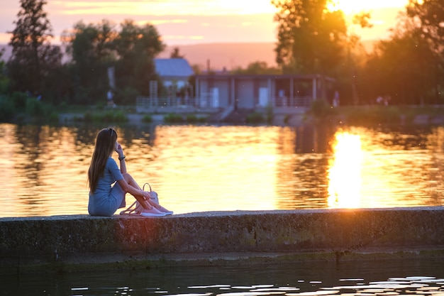 Premium Photo | Back view of lonely woman sitting on lake shore on warm ...