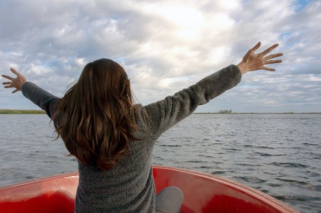 Back view of the young woman extending arms and enjoy on the boat and looking forward into lagoon Premium Photo