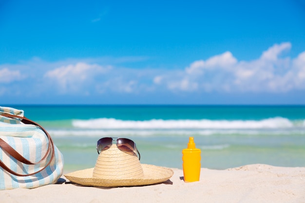Bag, straw hat with sunglasses and sunscreen lotion bottle on tropical sand Premium Photo