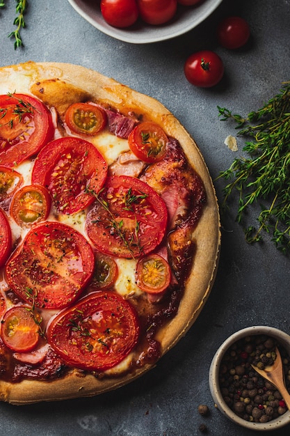 全粒生地 トマト ハム モッツァレラチーズ トマトソース タイムの焼きピザは 調理用のさまざまな食材を使用した灰色の石の背景に提供しています プレミアム写真