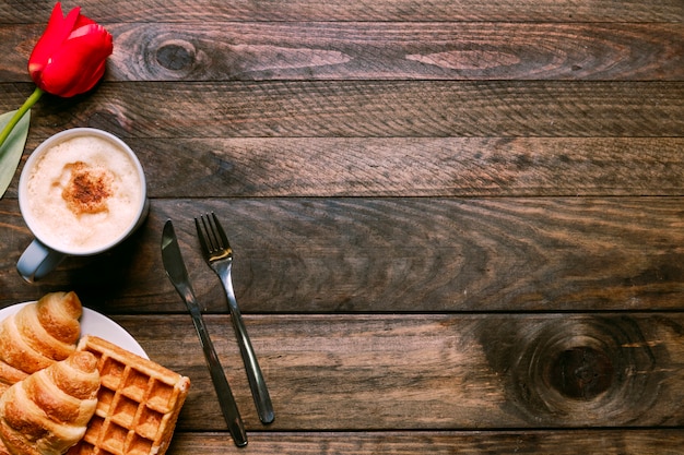 Bakery on plate near cup of drink, flower and cutlery Free Photo