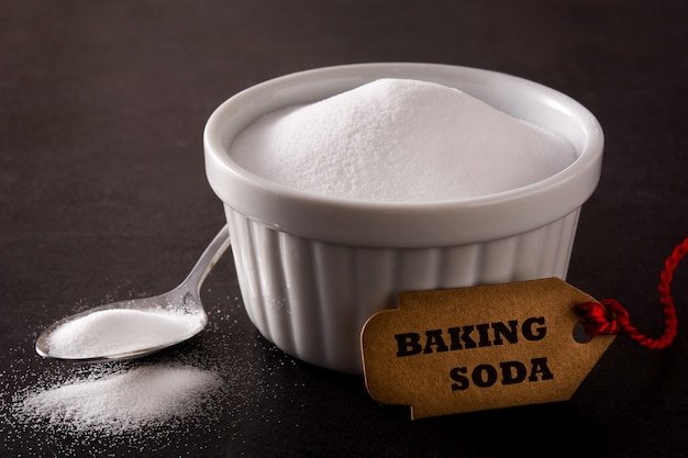 Baking soda in white bowl on black background Premium Photo