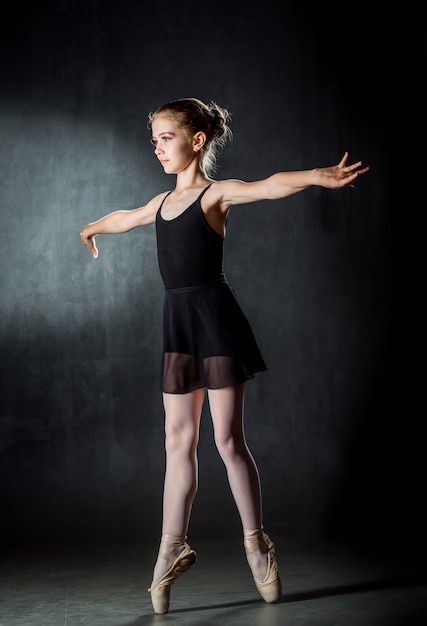 バレリーナ ポーズとスタジオで踊るかわいい女の子 リトルダンサー 暗い背景 黒い衣装 プレミアム写真