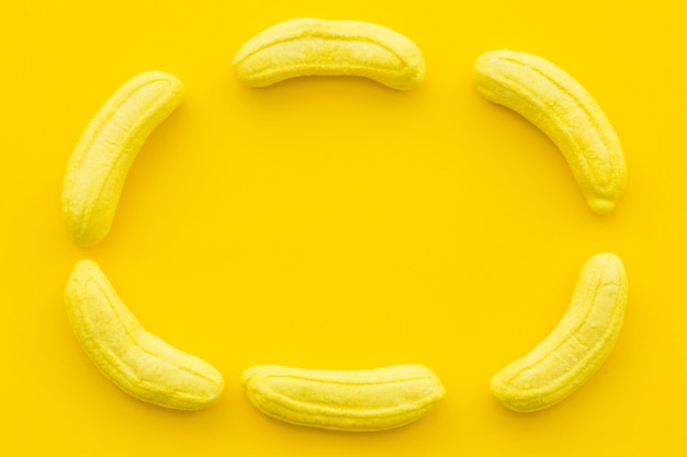 黄色の背景にフレームを形成するバナナ形キャンディー 無料の写真