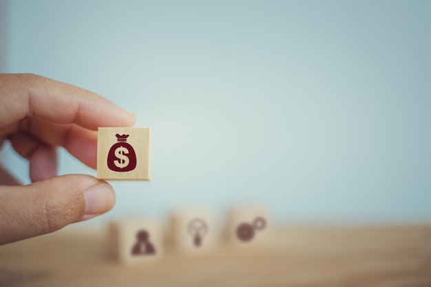 Banking and finance, financial planning concept: hand chooses wooden cube blocks with us dollar bags icons. management of corporate money to be consistent with the income in each quarter. Premium Photo