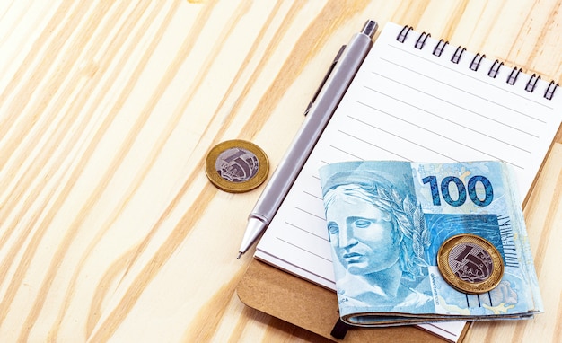 メモ帳とペンでテーブルに ブラジルのお金の紙幣と硬貨 プレミアム写真