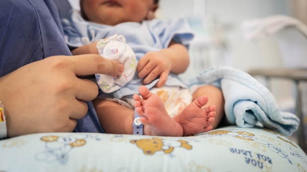 Bare feet of a cute newborn baby in a tender embrace of mother. Premium Photo