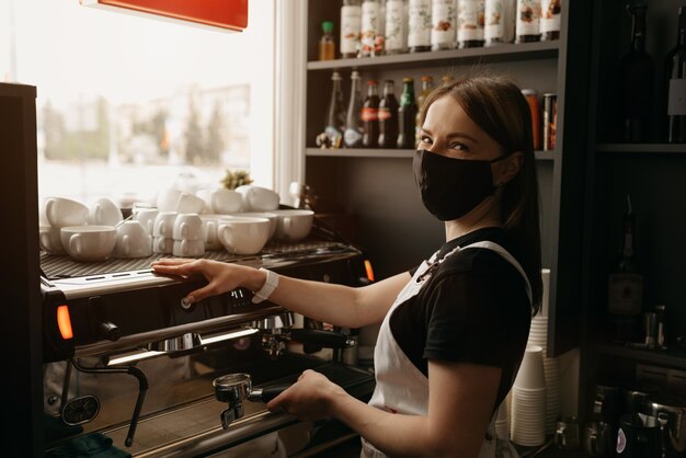 A barista in a face mask makes a cup of coffee in a cafe Premium Photo