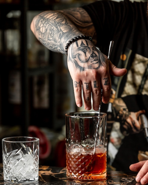 Free Photo | Bartender with tattoos making a red cocktail with whiskey.