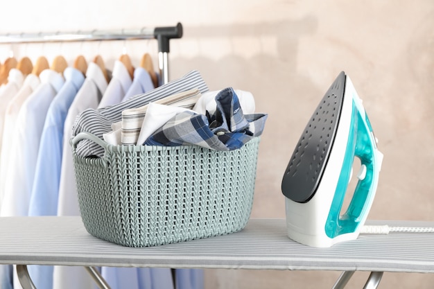 Premium Photo | Basket with clean laundry and iron on ironing board,