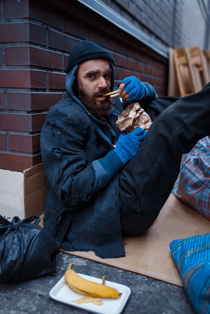 ひげを生やした乞食が街でハンバーガーを食べる プレミアム写真