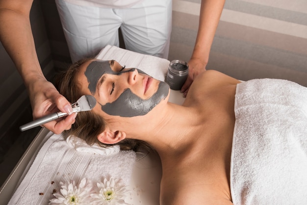 Beautician applying face mask with brush on woman's face Free Photo