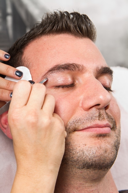 Beautician plucking a beautiful man  eyebrows with tweezers 