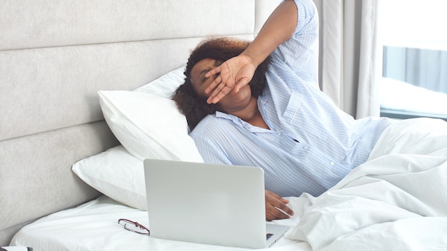 Beautiful african woman in stylish pajamas stretches while sitting in bed at home Premium Photo