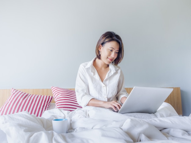 Beautiful Asian Women With Short Hair Wearing White Shirt Working With Laptop Computer On The Bed In The House Premium Photo