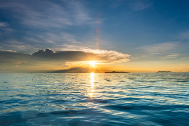 青い海と黄金の光空雲の背景と美しいビーチの夕日 プレミアム写真