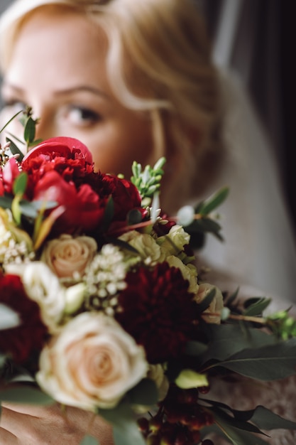 Beautiful blonde bride looks over dark red wedding bouquet