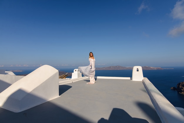 サントリーニ島 ティラの地中海を背景に家の屋根でポーズをとる白いドレスを着た美しい花嫁 プレミアム写真