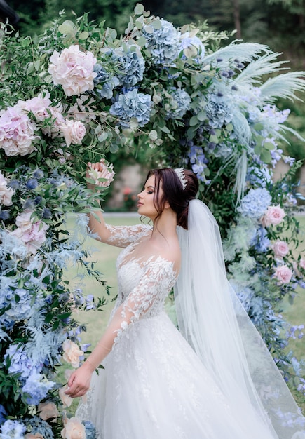 Free Photo Beautiful Caucasian Brunette Bride Is Standing Near The Archway Made Of Blue And Pink Hydrangea Outdoors