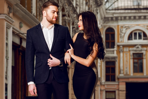 Beautiful elegant brunette with her husband  walking on the ale city streets . enjoying there time, wearing black classic suit and long cocktail dress. Free Photo