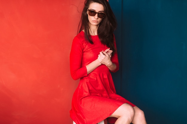 Premium Photo Beautiful Fashion Girl With Dark Long Hair Spanish Appearance In Sunglasses And Red Elegant Dress Posing On Blue Red Wall