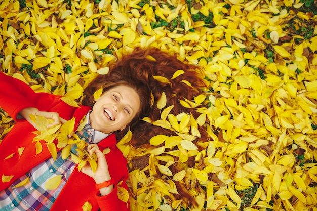 Beautiful happy woman laying in yellow autumn leaves. Free Photo