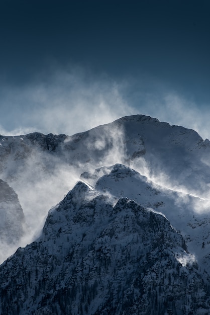 Beautiful high snowy and foggy mountains with snow being blown by wind ...