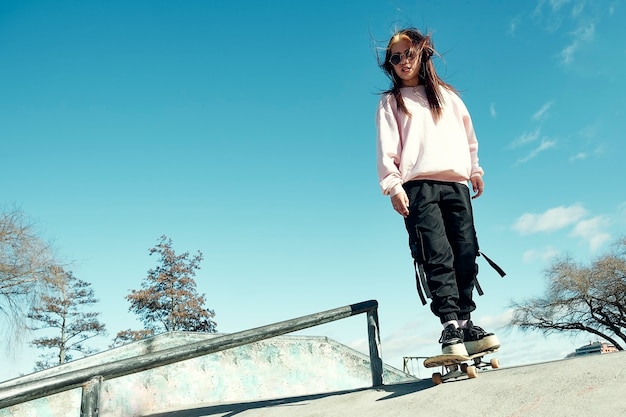 Beautiful hipster girl with casual clothes and long straight hair is skating on a ramp with her skateboard in the skate park Premium Photo